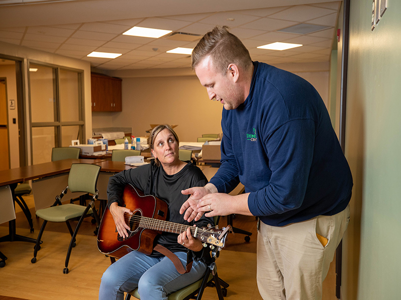 A music therapist helps a patient play guitar at StoneCrest Center